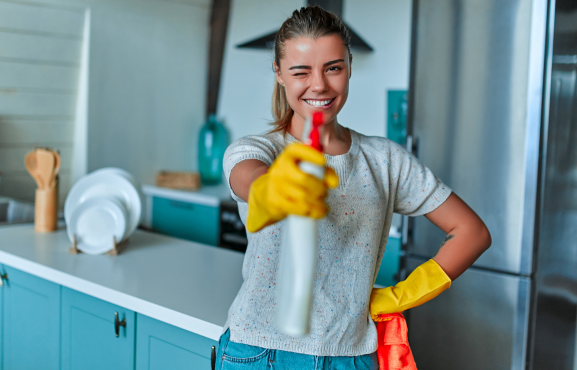 jeune femme un produit ménager à la main comme un pistolet dans une cuisine bleue