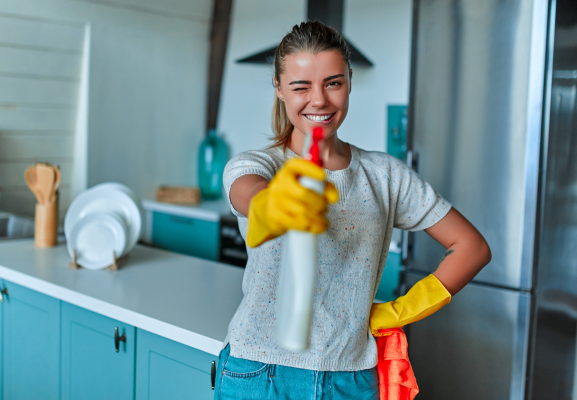 jeune femme un produit ménager à la main comme un pistolet dans une cuisine bleue
